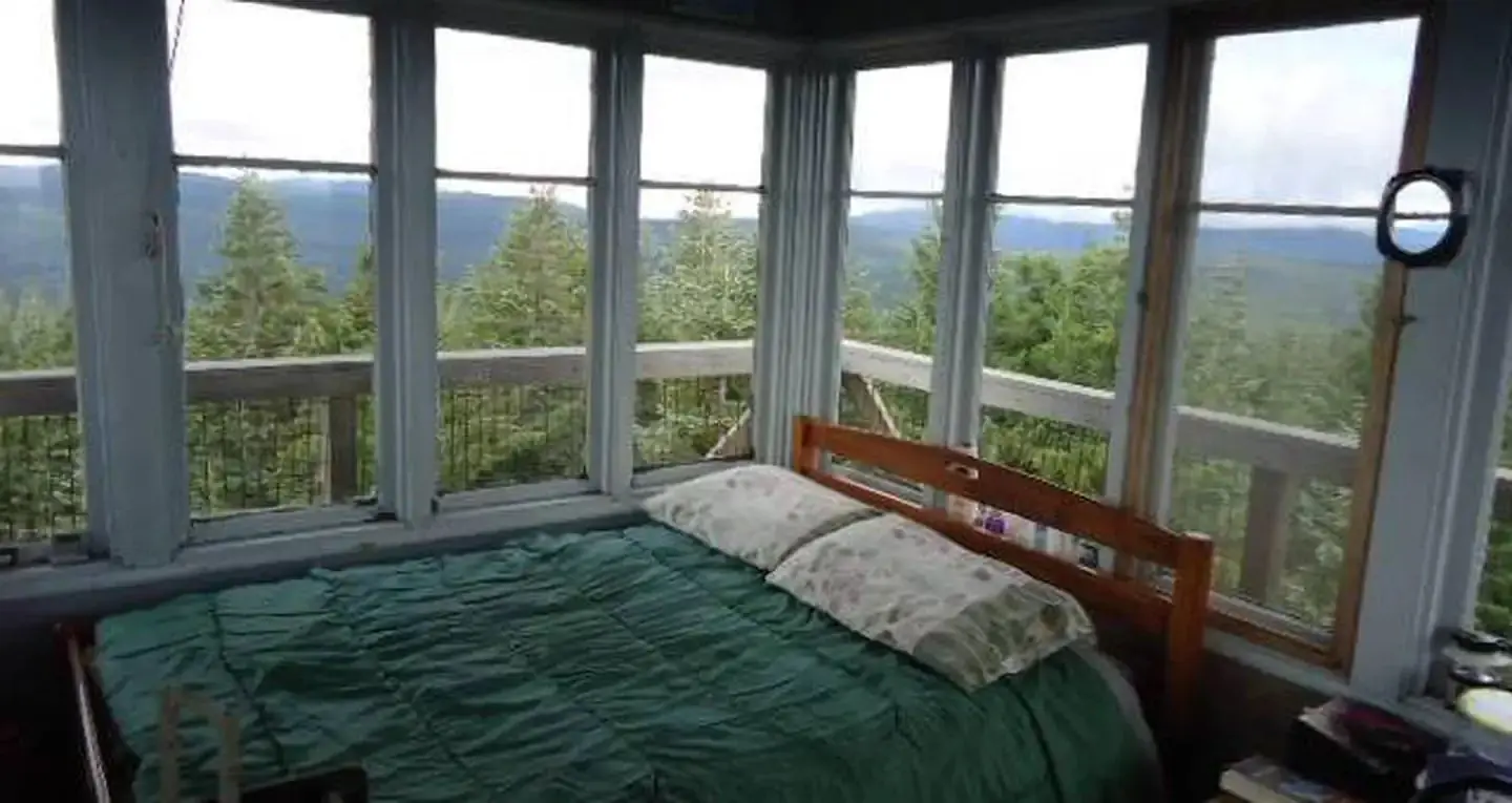 Full size bed in front of 8 window with view of mountains and trees beyond.