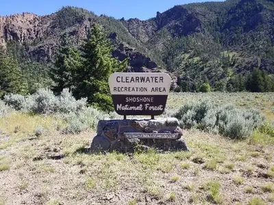 Yellow and brown campsite sign mounted on a rock pedestal. Trees, mountains and a little bit of blue sky are in the background.