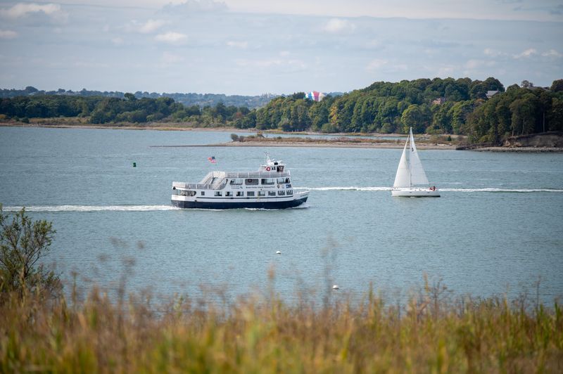 view from Spectacle Island overlooking the water with a public ferry and a sailboat