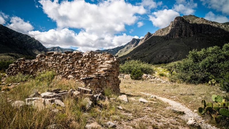A historic stone wall stands in ruins next to a hiking trail leading into the Guadalupe Mountains NP