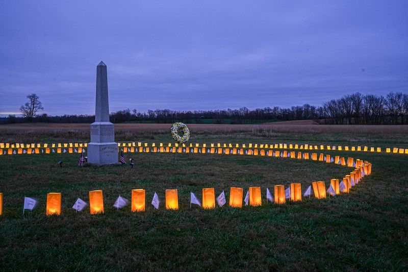 A stone obelisk in a grass field surrounded by luminary bags