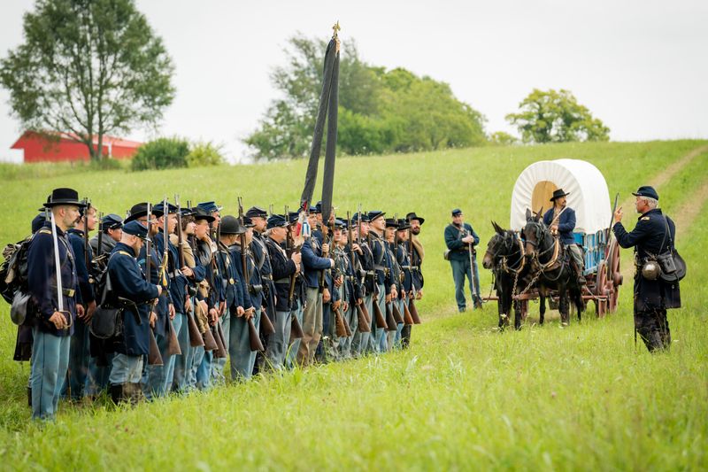 Living historians portraying US soldiers in a grass field with a wagon.