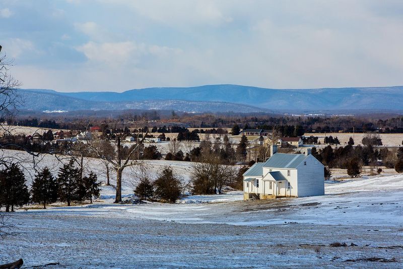 A white frame 1800s farmhouse stands alone in a snowy field.