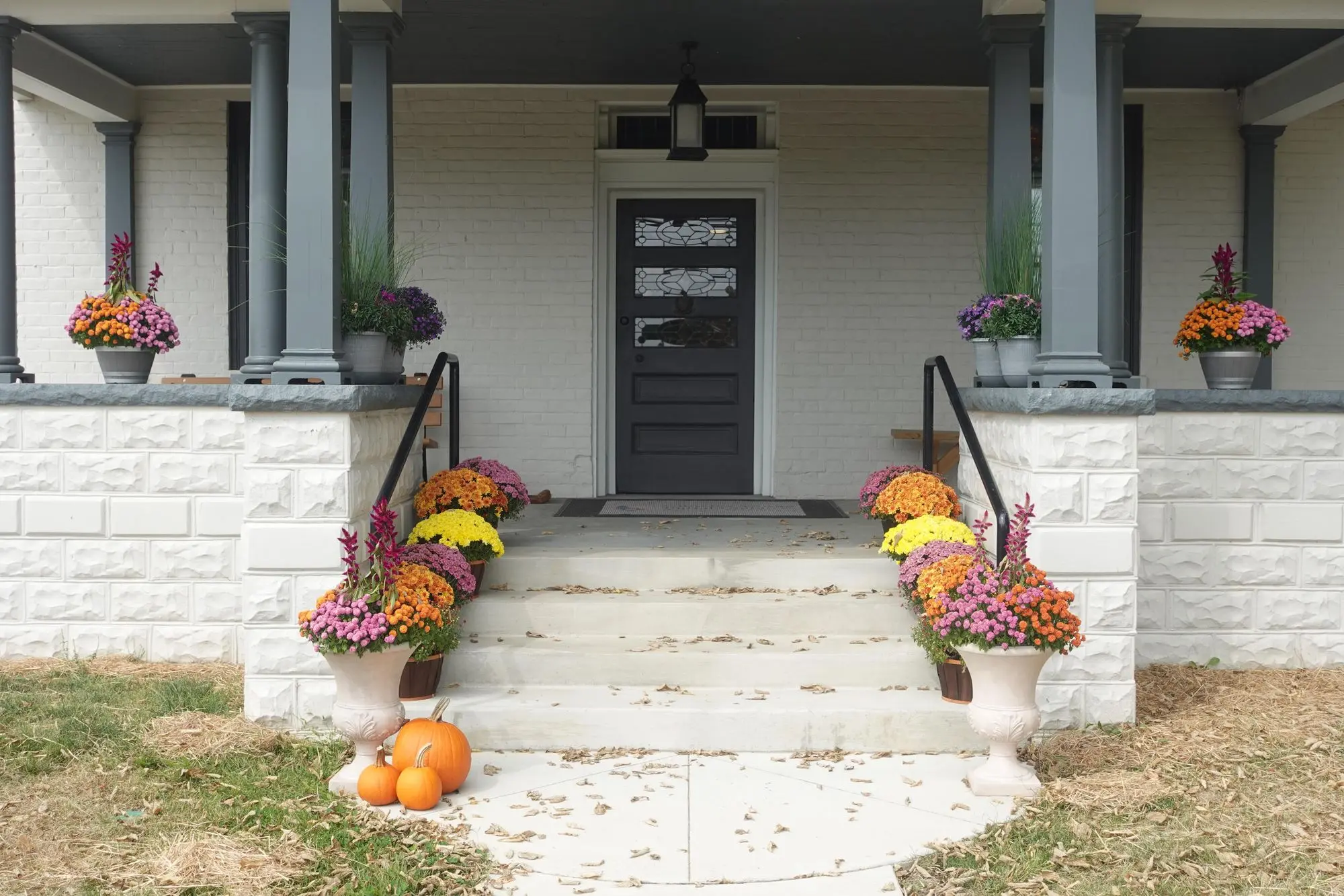 A large grey house with dark grey shutters with a green lawn out front under a blue sky