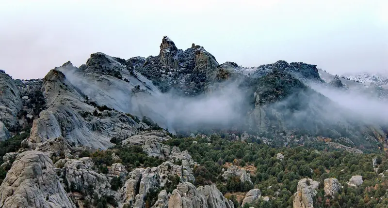 Snow dusted granite formations jut up from a mountainous juniper covered landscape.