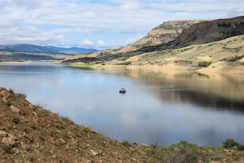 A single boat floating out in a reservoir. Mesas surrounding the area are reflected on the water.