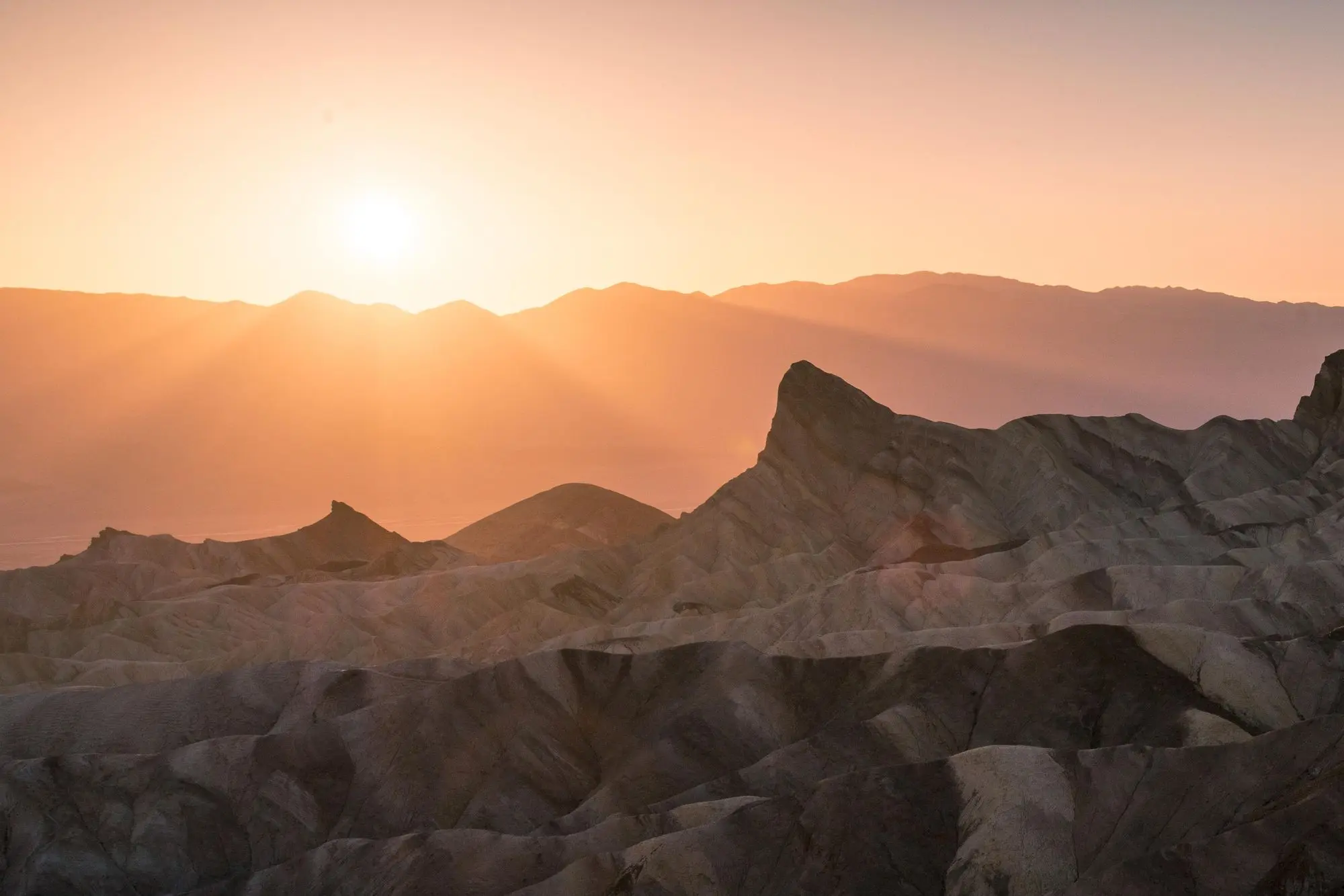 badlands bathed in pale pink and orange light from the setting sun
