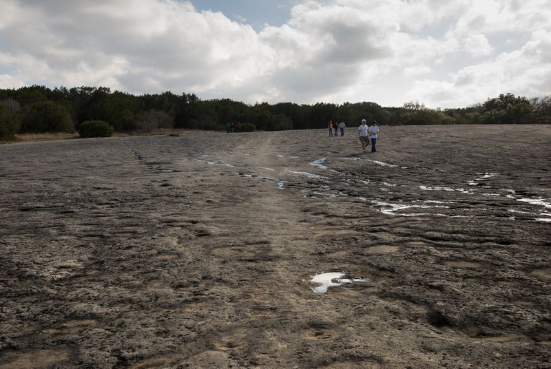 rock indentations in a dry creek with five people walking under clouds