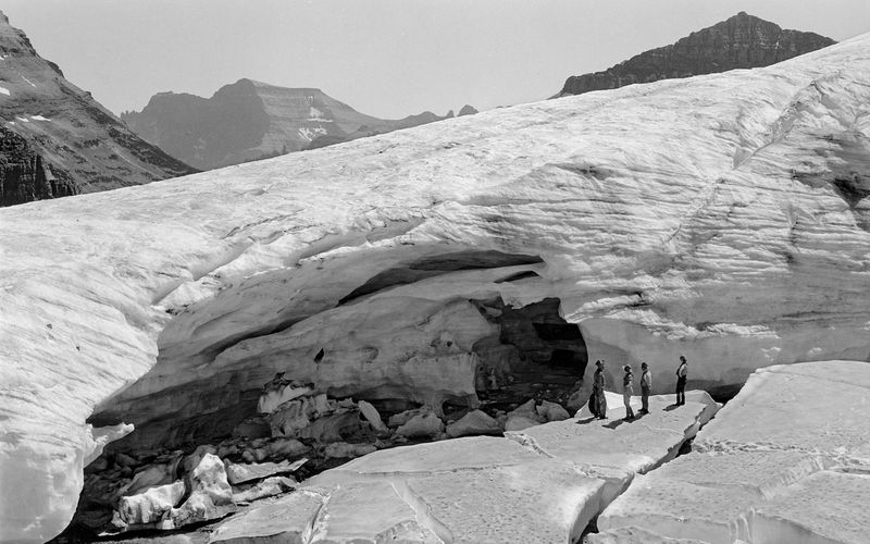 black and white picture of people standing near an ice cave in a glacier