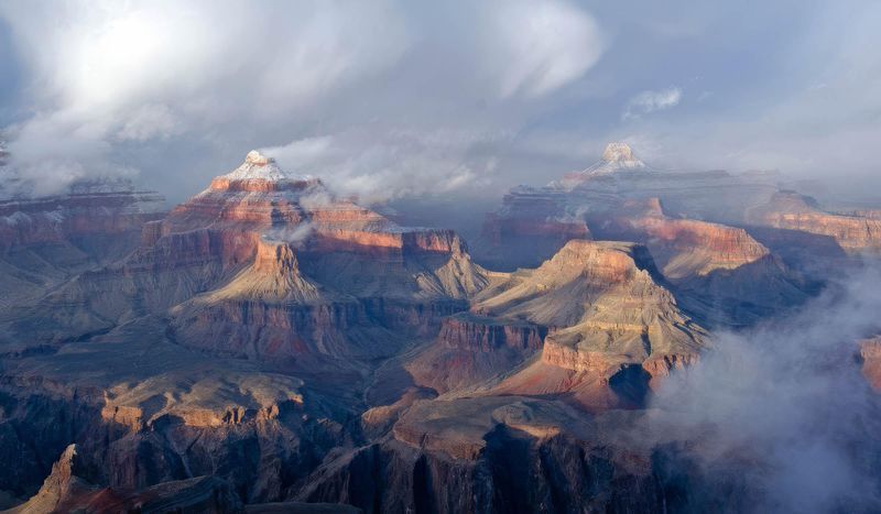 winter clouds and fog passing around a snow covered promentary within a vast mile deep canyon