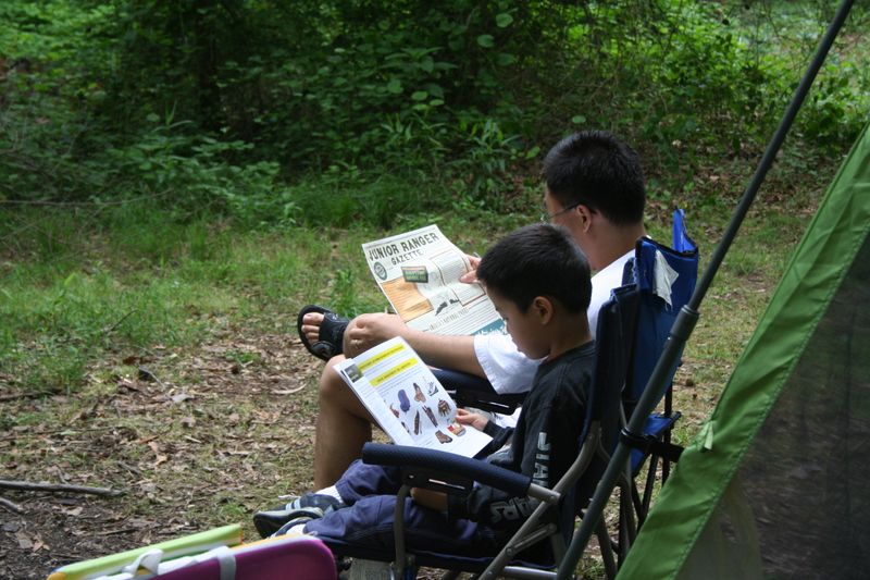 Father and son sitting in chairs reading in the Greenbelt Park campground