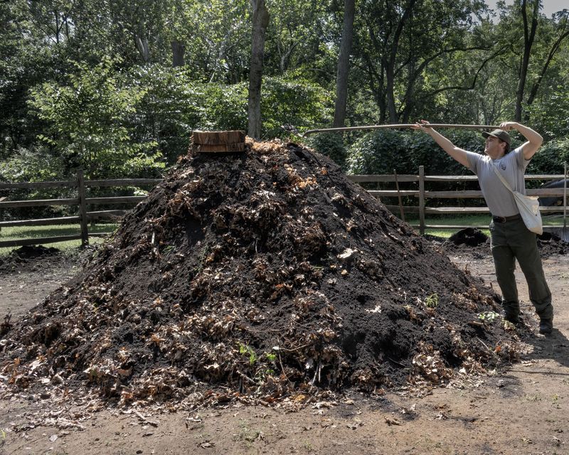 a large dirt pile with smoke coming out of the top. A park ranger scopes more dirt with a shovel.