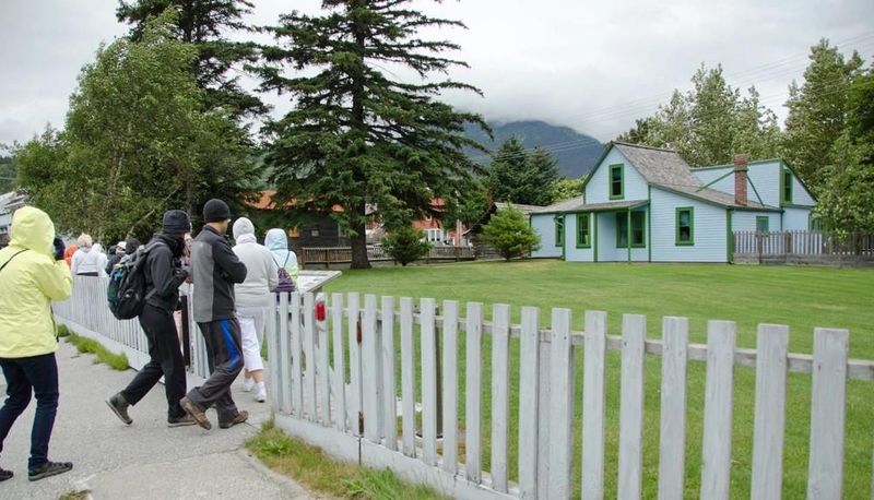 A pale blue building with green trim sits in front of a tidy lawn with a white picket fence.