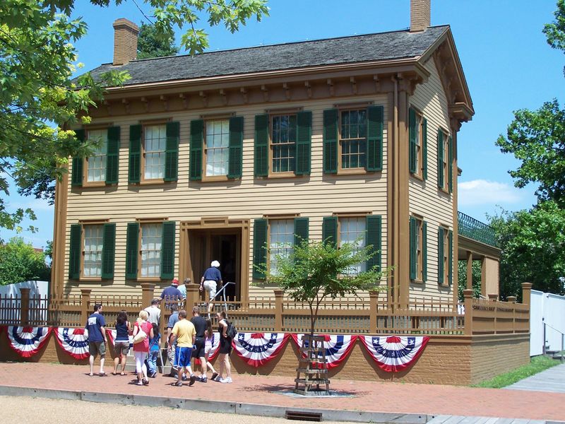 A guide leading a group into the Lincoln Home which has bunting on the front.
