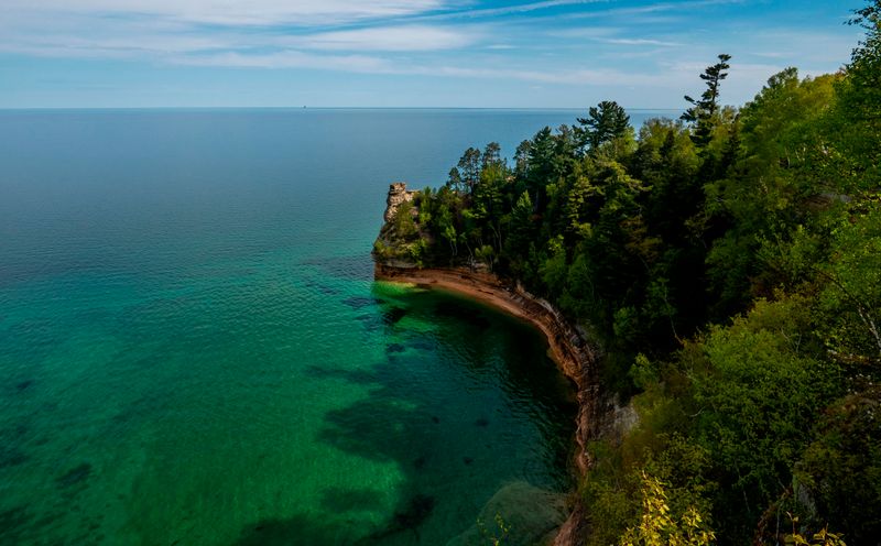A sandstone rock formation rises out of a blue-green Lake Superior on a sunny day.