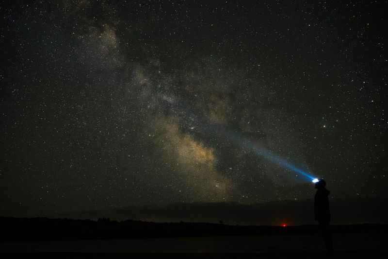 A person in a headlamp looks skyward at the milky way on a clear night