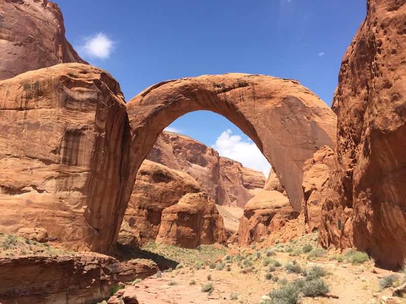 A large natural stone arch spans a red rock canyon.
