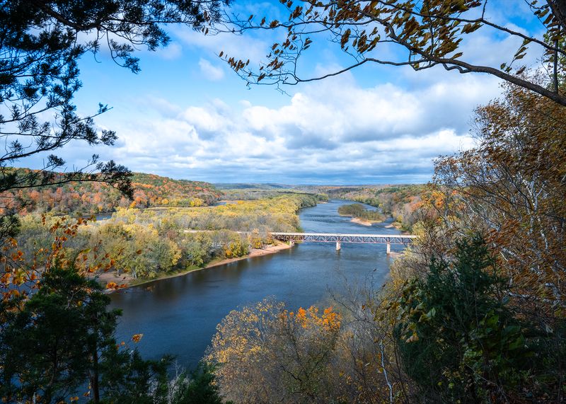 A blue river winds through a valley lined with trees in autumn color.
