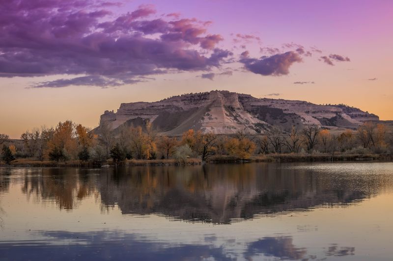 A pink sky and dramatic bluff are seen reflected in water.