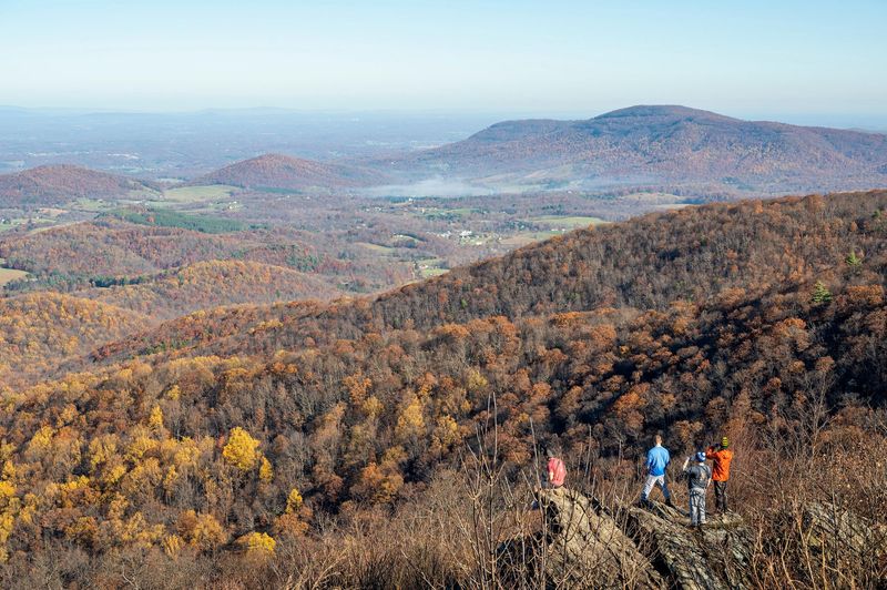 Visitors stand on a rocky outcrop overlooking the receding mountains.